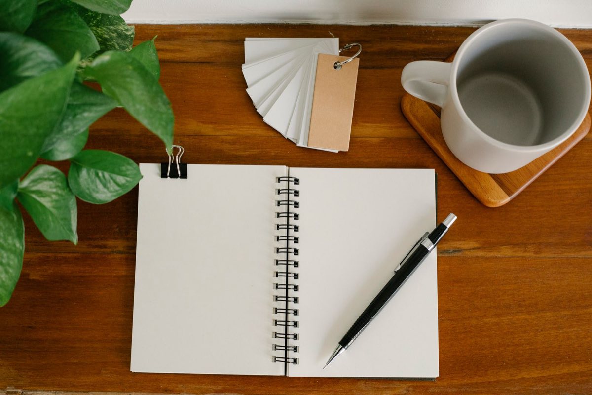 A desk with an open notebook, a ring of blank flip cards and a mug