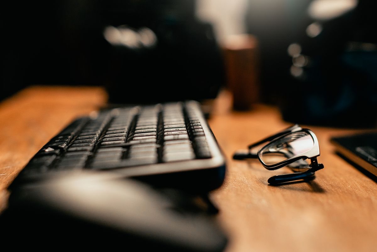 A computer keyboard and a pair of reading glasses on a warmly lit desk