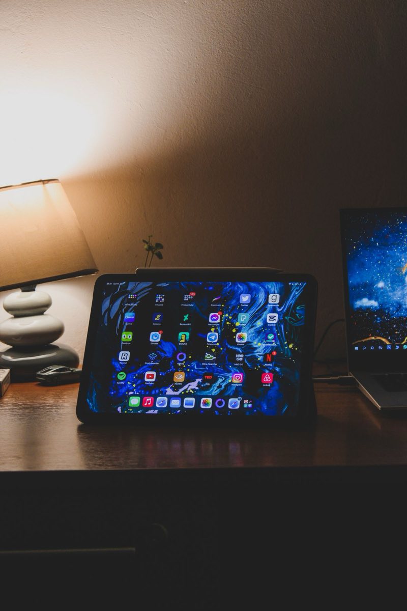 A tablet and laptop side by side under a warm lamp