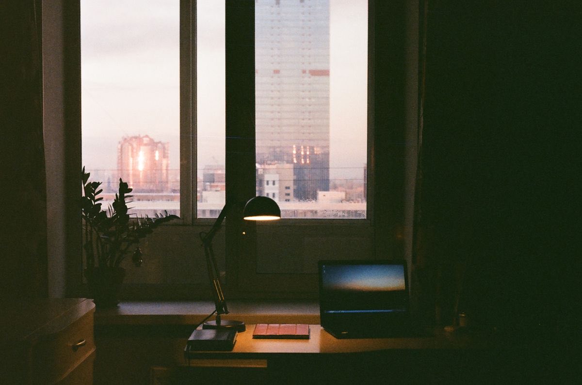 An empty desk with a laptop and lamp, dusk through the window